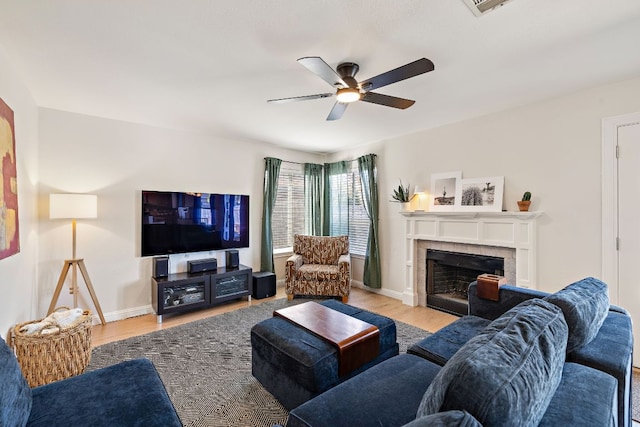 living room with a fireplace, baseboards, light wood-type flooring, and a ceiling fan