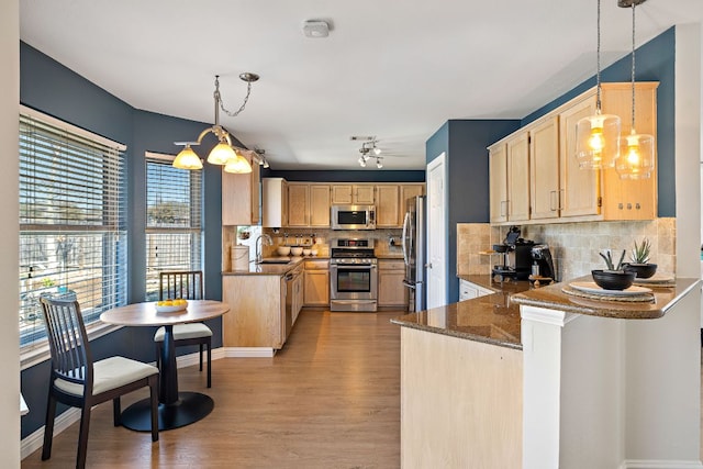 kitchen with light brown cabinets, a sink, dark stone counters, appliances with stainless steel finishes, and a peninsula