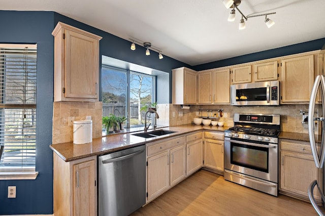 kitchen with light brown cabinets, a sink, stainless steel appliances, light wood finished floors, and decorative backsplash