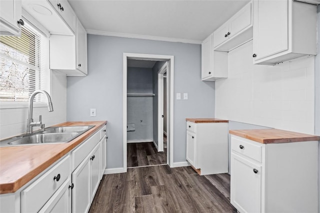 kitchen with a sink, dark wood-type flooring, white cabinets, wood counters, and crown molding