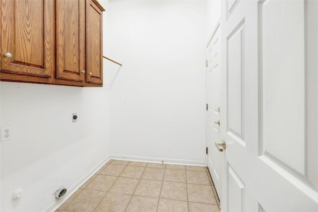 washroom featuring electric dryer hookup, baseboards, cabinet space, and light tile patterned floors