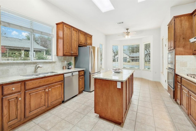 kitchen with brown cabinetry, visible vents, a kitchen island, a sink, and appliances with stainless steel finishes