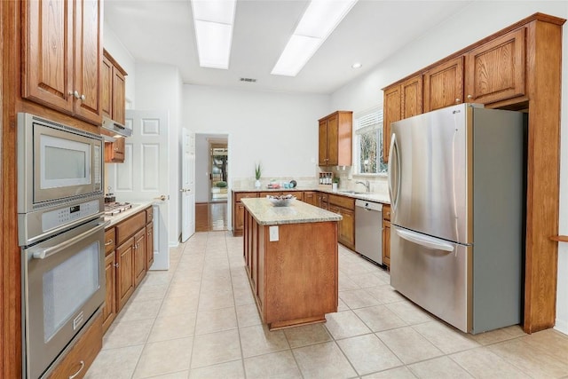 kitchen featuring brown cabinets, a sink, a center island, appliances with stainless steel finishes, and light tile patterned floors