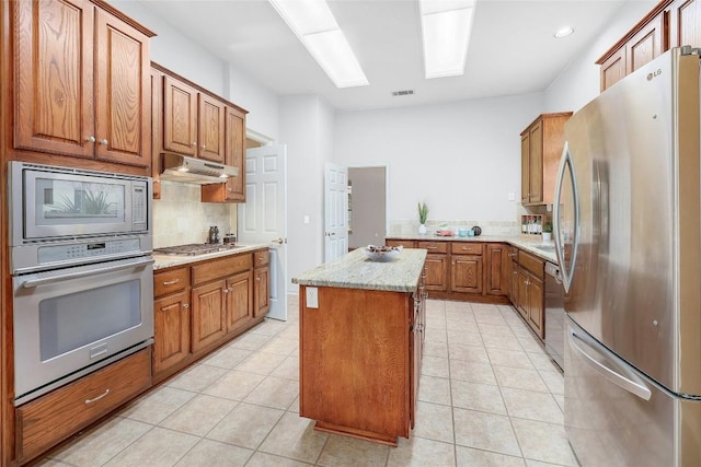 kitchen with brown cabinets, under cabinet range hood, a kitchen island, stainless steel appliances, and a skylight