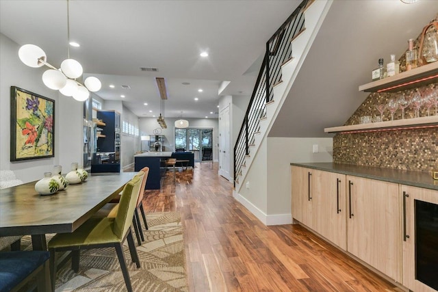 dining space featuring baseboards, light wood finished floors, stairs, wine cooler, and a dry bar