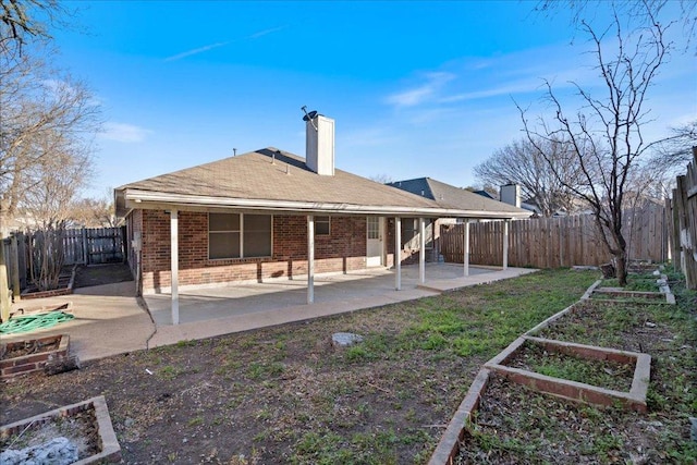 rear view of property with brick siding, a chimney, a fenced backyard, a patio area, and a vegetable garden