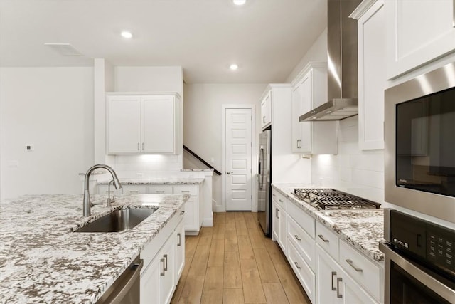 kitchen featuring light wood-type flooring, a sink, appliances with stainless steel finishes, white cabinets, and wall chimney range hood