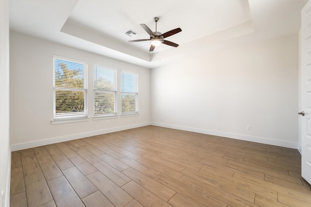 unfurnished room featuring light wood-type flooring, a tray ceiling, and baseboards