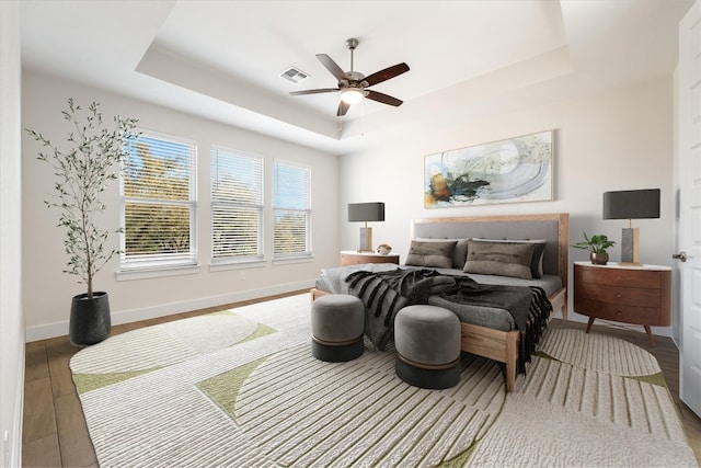 bedroom featuring a tray ceiling, baseboards, and wood finished floors