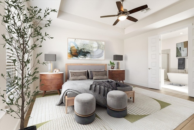 bedroom with a raised ceiling, baseboards, visible vents, and ensuite bathroom