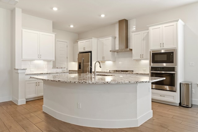 kitchen with white cabinets, appliances with stainless steel finishes, wall chimney range hood, and a sink