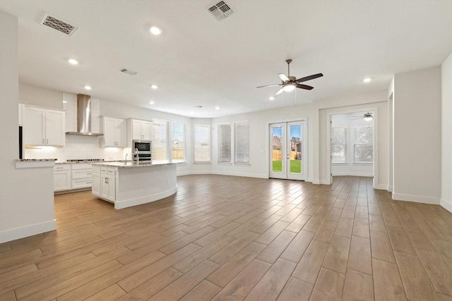 kitchen featuring open floor plan, visible vents, light wood finished floors, and wall chimney range hood