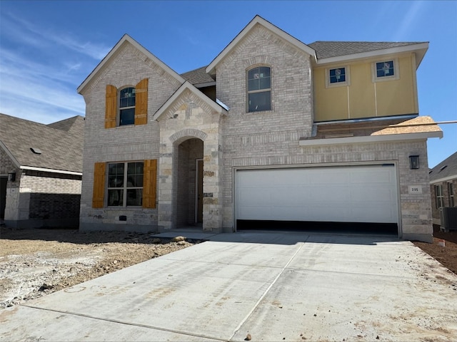 french country home featuring roof with shingles, an attached garage, concrete driveway, stone siding, and brick siding