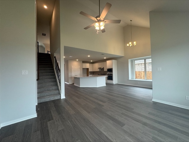 191 Dove Tree Dr, Buda, TX 78610 - unfurnished living room featuring high vaulted ceiling, dark wood-type flooring, stairs, baseboards, and ceiling fan with notable chandelier