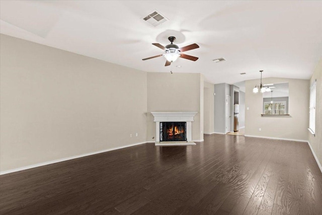 unfurnished living room with dark wood finished floors, baseboards, visible vents, and a warm lit fireplace