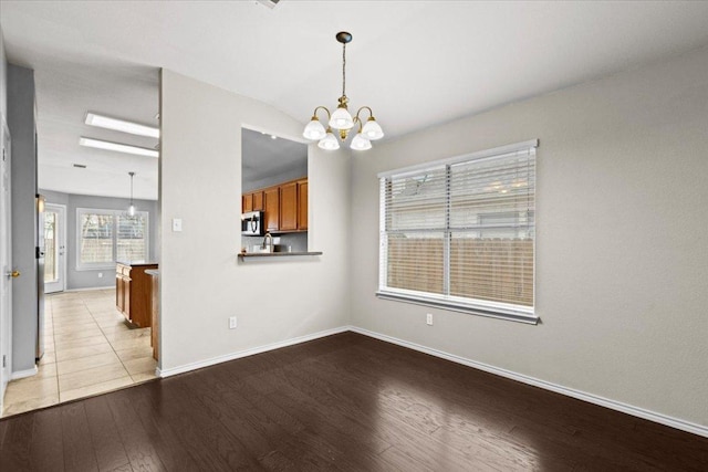 unfurnished dining area featuring lofted ceiling, light wood-style flooring, a notable chandelier, and baseboards