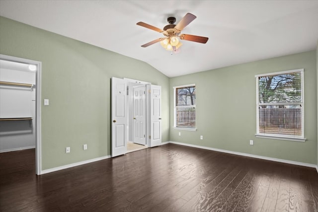 unfurnished bedroom with a walk in closet, multiple windows, lofted ceiling, and wood finished floors