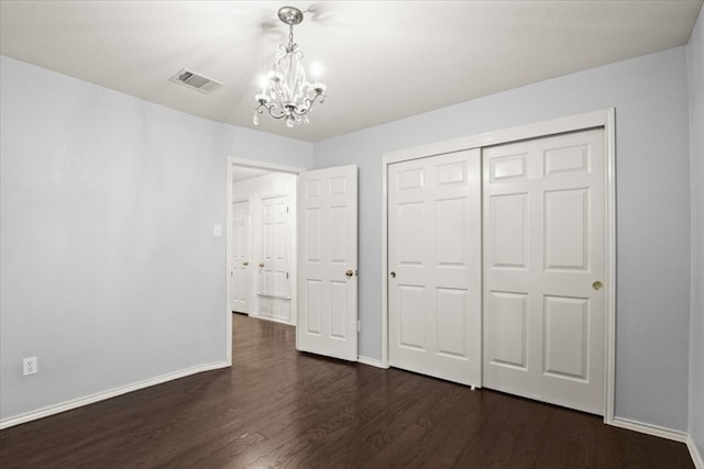 unfurnished bedroom featuring baseboards, visible vents, dark wood finished floors, a closet, and a notable chandelier