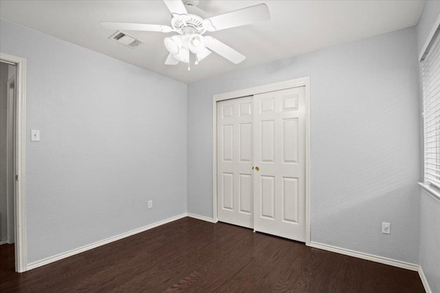 unfurnished bedroom with dark wood-style floors, visible vents, a closet, and baseboards