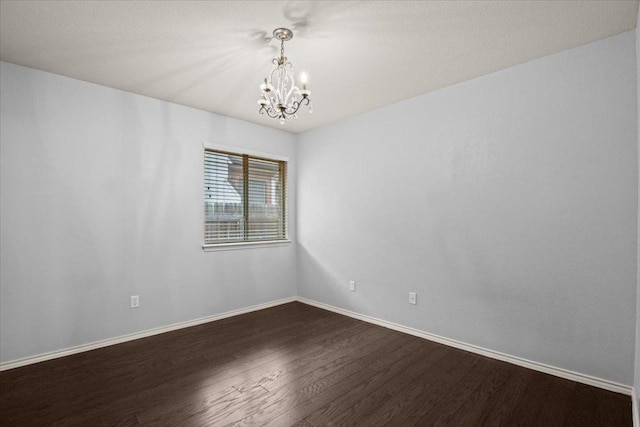 unfurnished room with a notable chandelier, baseboards, and dark wood-style flooring