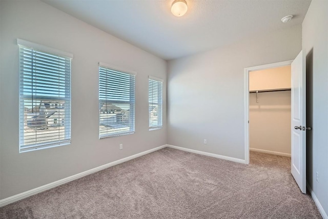 unfurnished bedroom featuring a spacious closet, a closet, baseboards, and carpet