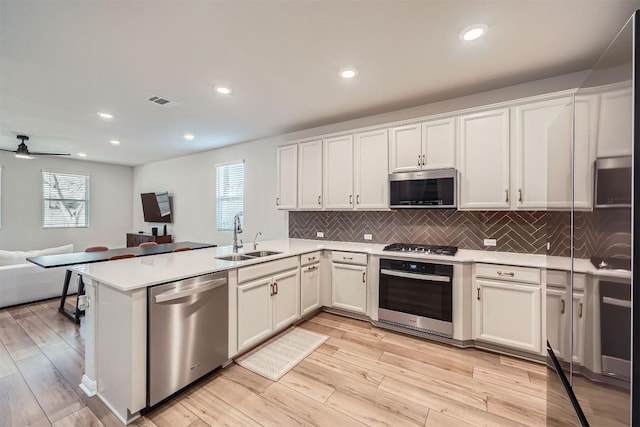 kitchen with a sink, open floor plan, a peninsula, appliances with stainless steel finishes, and light countertops