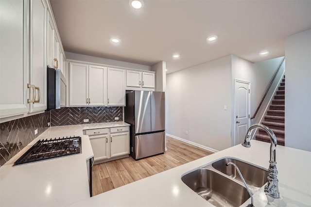 kitchen featuring a sink, light countertops, light wood-style floors, appliances with stainless steel finishes, and tasteful backsplash