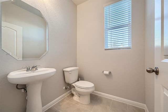 half bath featuring tile patterned floors, toilet, and baseboards