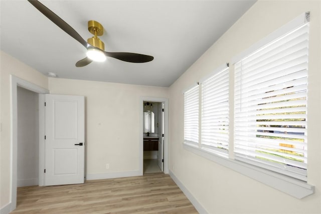 unfurnished bedroom featuring ceiling fan, baseboards, light wood-style floors, and ensuite bath