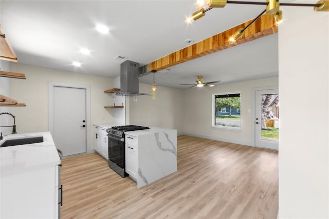 kitchen with stainless steel gas range, open shelves, light wood-style flooring, a sink, and island range hood