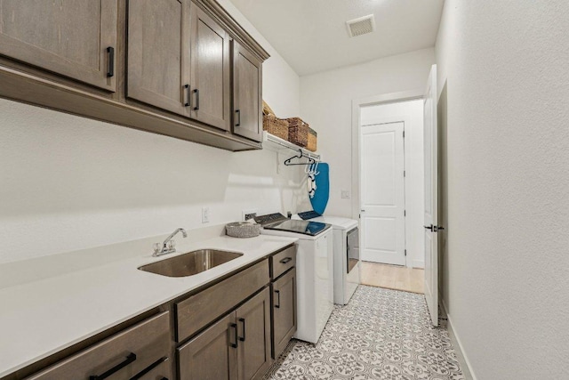 clothes washing area featuring visible vents, a sink, cabinet space, separate washer and dryer, and baseboards