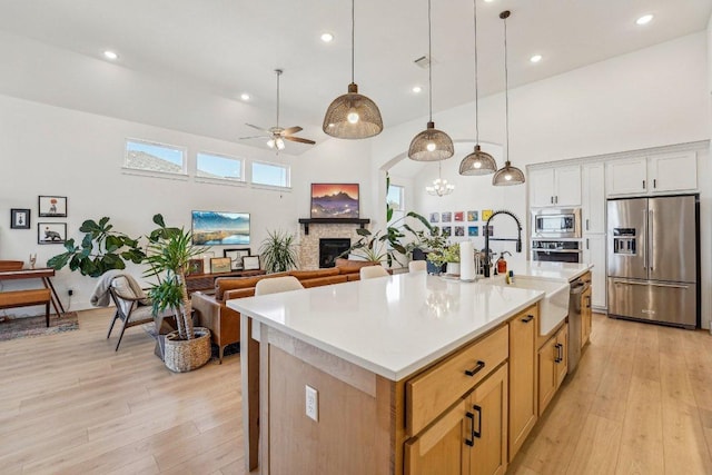 kitchen featuring a glass covered fireplace, stainless steel appliances, a high ceiling, and light wood-type flooring