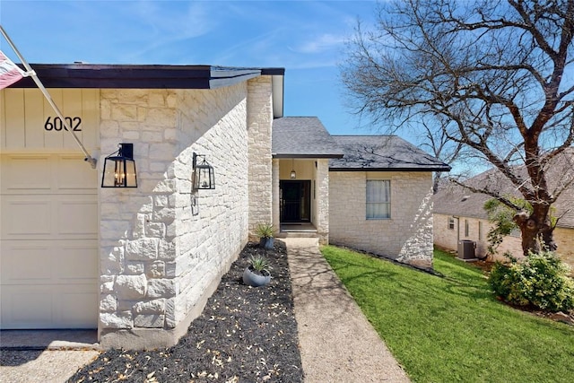 view of front of property featuring a front yard, central AC, a shingled roof, stone siding, and a garage