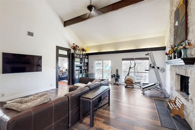 living area featuring wood finished floors, visible vents, high vaulted ceiling, beam ceiling, and a stone fireplace