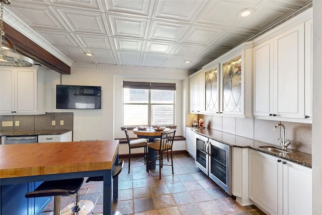 kitchen with a sink, an ornate ceiling, backsplash, stainless steel dishwasher, and baseboards