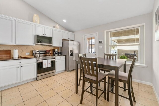 kitchen featuring dark countertops, backsplash, lofted ceiling, light tile patterned floors, and stainless steel appliances