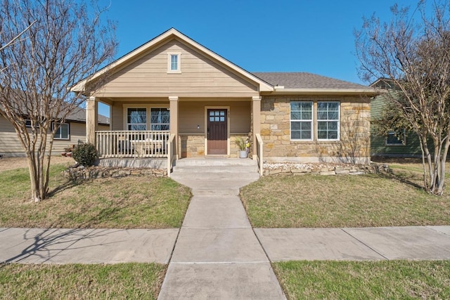 view of front of property with a front yard, covered porch, stone siding, and a shingled roof