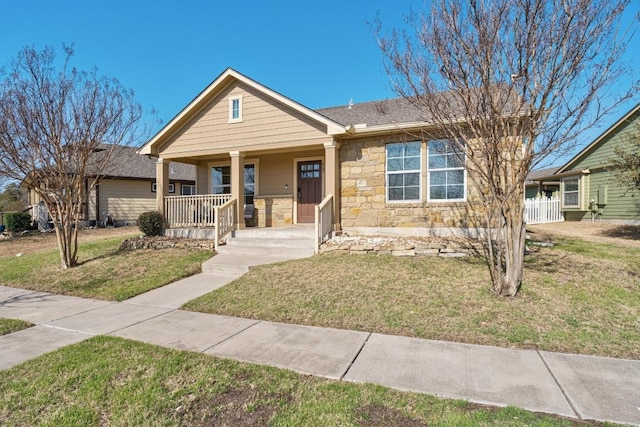 view of front of house featuring a porch, stone siding, a front yard, and a shingled roof