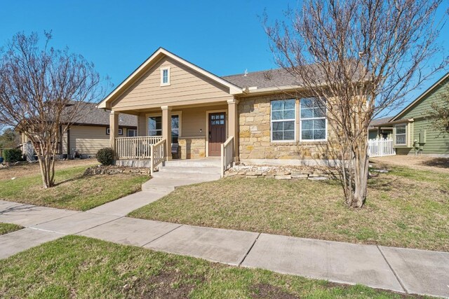 view of front of house featuring a porch, stone siding, a front yard, and a shingled roof