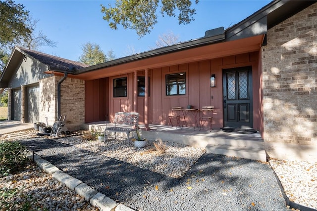 property entrance featuring driveway, brick siding, covered porch, a garage, and board and batten siding