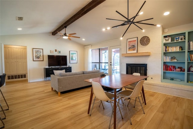 dining room with visible vents, light wood-style flooring, a fireplace, and vaulted ceiling with beams