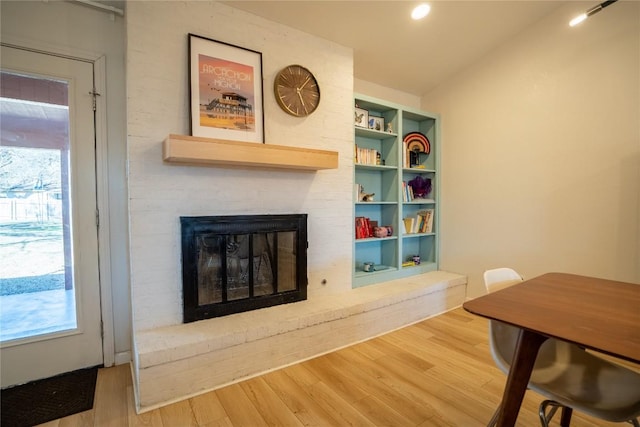 living room with built in features, a healthy amount of sunlight, a brick fireplace, and wood finished floors