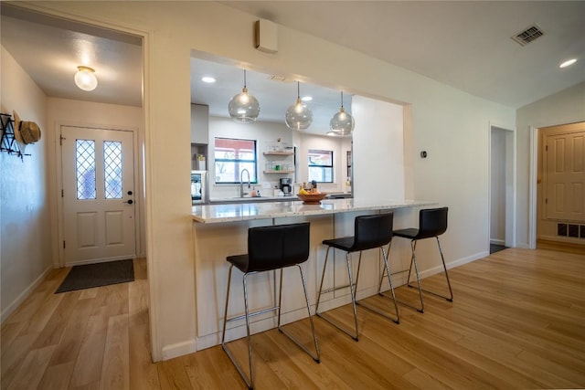 kitchen with light stone counters, visible vents, a breakfast bar, and light wood-style flooring