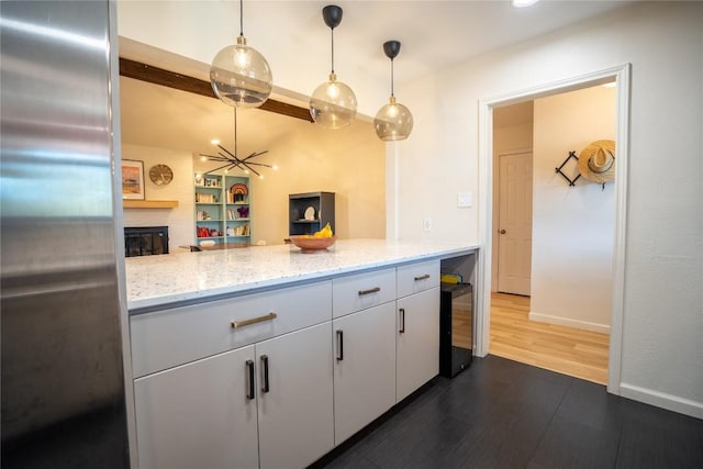 kitchen with dark wood-type flooring, pendant lighting, beverage cooler, stainless steel refrigerator, and a fireplace