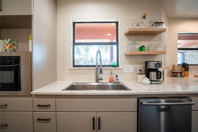 kitchen with a sink, black oven, light stone countertops, and dishwasher