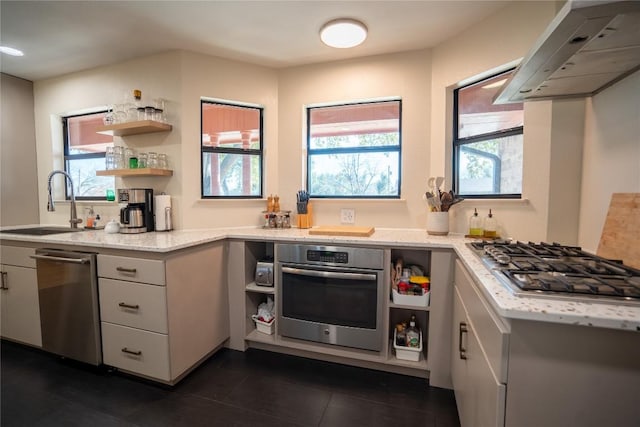 kitchen with light stone countertops, open shelves, a sink, appliances with stainless steel finishes, and wall chimney range hood