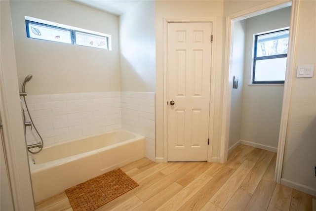 bathroom with a bath, baseboards, and wood finished floors