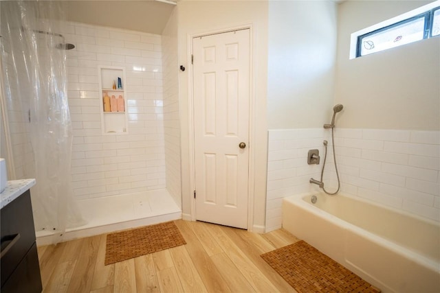 bathroom with vanity, a bath, wood finished floors, and tiled shower