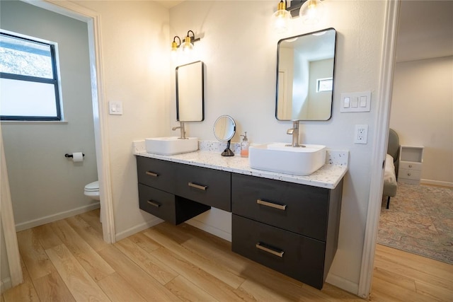 ensuite bathroom with double vanity, toilet, wood finished floors, and a sink