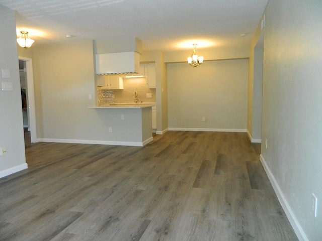 unfurnished living room with a chandelier, baseboards, and wood finished floors